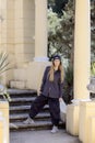 A girl in wide trousers and a shirt stands near the steps against the background of columns. Hiphop in classical