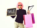 Girl in wig holding package, hangers, board with sale inscription