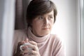 Girl at the window with a cup in winter. Home, sweater. Young Woman Enjoying her morning coffee or tea Royalty Free Stock Photo