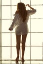 The girl at the window in the morning. silhouette. a woman in a man`s shirt at dawn