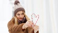 Girl in winter clothes and a hat holds two caramel candy canes and making heart shape. Royalty Free Stock Photo