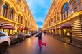 Girl in winter clothes posing at the beginning of a long street with buildings decorated with festoons. New Year decorated city