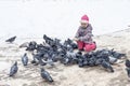 A girl in winter clothes sat down and feeds pigeons with crumbs. saving the pitz from starvation in winter