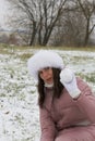 A girl in winter clothes on a walk in the park. Holds a ball of snow in his hand. The ground is covered with the first snow