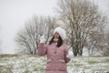 A girl in winter clothes on a walk in the park. Holds a ball of snow in his hand. The ground is covered with the first snow