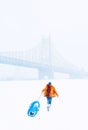 Girl with a winter coat grabbing luggage on snow ground with long bridge on the horizon