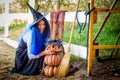 A girl in a witch costume, celebrating Halloween, sat down by a pumpkin with a drawn malicious grimace