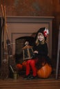 A girl in a witch costume sits near the fireplace on a pumpkin, holding a lantern in her hands Royalty Free Stock Photo