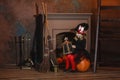 A girl in a witch costume sits near the fireplace on a pumpkin, holding a lantern in her hands Royalty Free Stock Photo