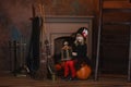 A girl in a witch costume sits near the fireplace on a pumpkin, holding a lantern in her hands Royalty Free Stock Photo