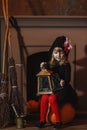 A girl in a witch costume sits near the fireplace on a pumpkin, holding a lantern in her hands Royalty Free Stock Photo