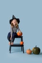 Girl in witch hat and black clothes sits on stepping stool with pumpkin in hand Royalty Free Stock Photo