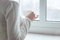 Girl woman in the morning holding a cup with hot tea or coffee and looking at the window in her home and having a relax time. Royalty Free Stock Photo