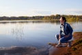 Girl or woman sitting on the shore or beach of the lake in the evening at sunset. Single trip or vacation