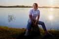 Girl or woman sitting on the shore or beach of the lake in the evening at sunset. Single trip or vacation