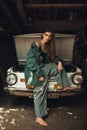 Girl worker in overalls stands in workshop near opened capote of