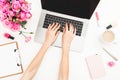 Girl working on laptop. Office workspace with female hands, laptop, pink roses bouquet, coffee mug, diary on white table. Top view