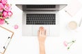 Girl working on laptop. Woman workspace with female hands, laptop, pink roses bouquet, coffee mug, diary on white table. Top view.