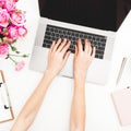 Girl working on laptop. Workspace with female hands, laptop, roses bouquet and diary on white table. Top view. Flat lay.