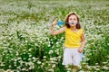 A girl with a wreath of daisies on her head in the field playing and blowing soap bubbles in nature. A large chamomile field on a Royalty Free Stock Photo