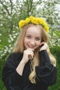 A girl of 13 with a wreath of dandelions in a spring flowering garden. The girl smiles and looks at the camera
