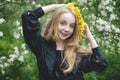 A girl of 13 with a wreath of dandelions in a spring flowering garden. The girl smiles and looks at the camera