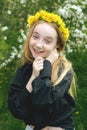 A girl of 13 with a wreath of dandelions in a spring flowering garden. The girl smiles and looks at the camera