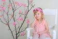 girl in a wreath of flowers in pink dress sitting on a chair smiling, hand propping cheek Royalty Free Stock Photo