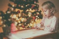 Girl writes a letter to Santa near the New Year tree at the table, soft focus