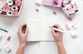 Girl writes in open notebook on table with flowers and marshmallows,pastel colors.Beauty Flat lay.Copy space.Eye bird view. Royalty Free Stock Photo