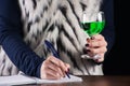 Girl writing in notebook and holds Absinthe alcohol drink in hand Royalty Free Stock Photo