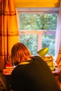 Girl writting at table with green lamp near the wooden window in country house interior Royalty Free Stock Photo