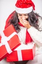 Girl in a Xmas hat opens up a Christmas present and holds hand in front of her mouth from the surprise Royalty Free Stock Photo