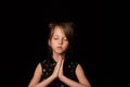 A girl of 6 years, against a dark background. A gesture of prayer and gratitude.The palms are folded, the eyes are