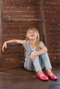 Girl 6 years old in jeans and a vest sits on the floor next to brick wall. filled with laughter