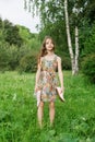 Girl of 10 years old stands on the grass and holds shoes in her hands in the summer