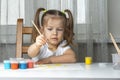 girl 3-4 years old with two ponytails in a white T-shirt draws paints at the table Royalty Free Stock Photo