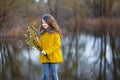 A girl in a yellow coat in the forest in early spring with a willow branch of twigs. A girl furing freshet or high water