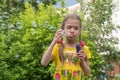 A girl in a yellow dress blows soap bubbles in a park against a background of trees. Cute little girl blowing soap