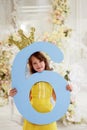 A girl in a yellow dress holds a large number 6.With a Golden crown. The Princess birthday party. Royalty Free Stock Photo