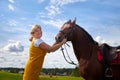 Girl in yellow dress with a horse on a green field and a blue sky with white clouds on the background Royalty Free Stock Photo