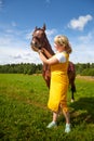 Girl in yellow dress with a horse on a green field and a blue sky with white clouds on the background Royalty Free Stock Photo