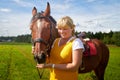 Girl in yellow dress with a horse on a green field and a blue sky with white clouds on the background Royalty Free Stock Photo