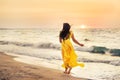 A girl in a yellow dress with long hair runs along the seashore