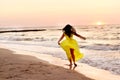 A girl in a yellow dress with long hair runs along the seashore