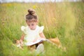 Girl in a yellow dress sits in the grass on a blanket in a field and reads a paper book. International Children`s Day. Summer tim Royalty Free Stock Photo