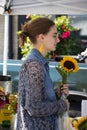 Girl with yellow earrings and denium blouse and glasses holds a sunflower at Cherry Street farmers market