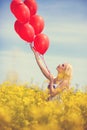 Girl in yellow field letting go of a bunch of balloons Royalty Free Stock Photo