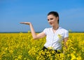 Girl in yellow flower field. Show palm. Hold in palm of something and smile. Beautiful spring landscape, bright sunny day, rapesee Royalty Free Stock Photo