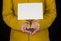 Girl in yellow holds coins in hands and clean sheet for writing, black background, close-up Royalty Free Stock Photo